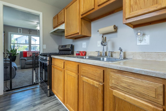 kitchen with a sink, light countertops, wood finished floors, gas range, and under cabinet range hood