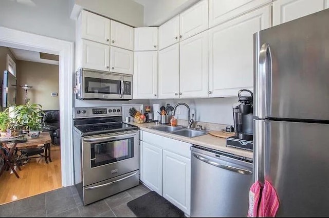 kitchen featuring tile patterned flooring, light countertops, white cabinets, a sink, and appliances with stainless steel finishes