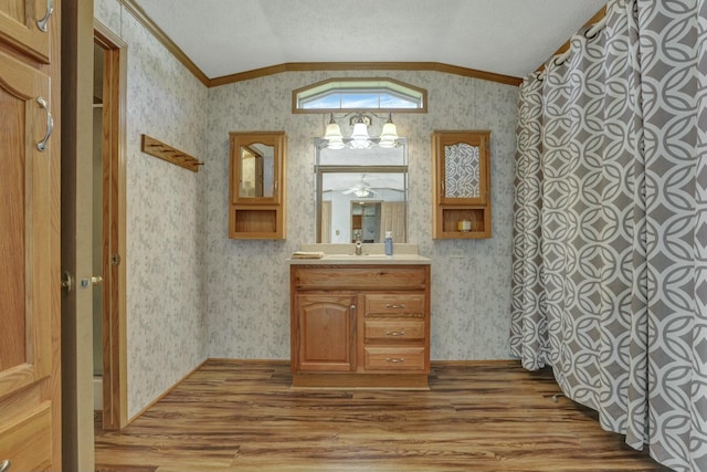 bathroom featuring vanity, wood finished floors, wallpapered walls, and vaulted ceiling
