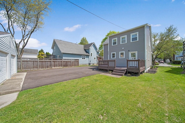 rear view of house featuring a yard, fence, a wooden deck, and aphalt driveway
