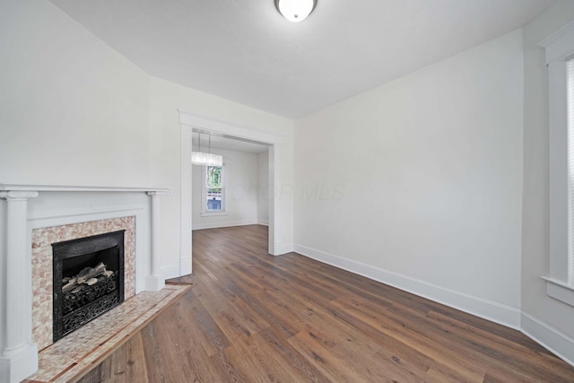 unfurnished living room with a fireplace, baseboards, a chandelier, and dark wood-type flooring