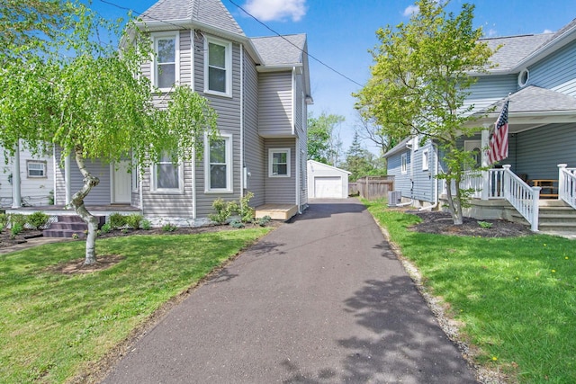 victorian house with an outdoor structure, a front lawn, covered porch, central AC unit, and a detached garage