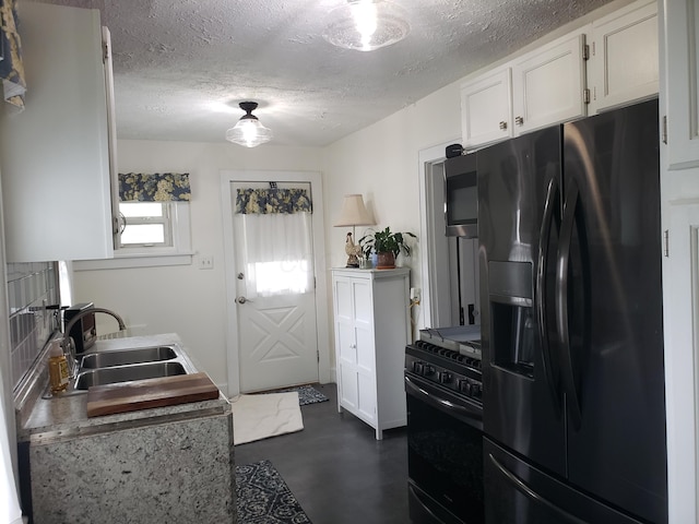 kitchen featuring a textured ceiling, finished concrete floors, a sink, white cabinets, and black appliances