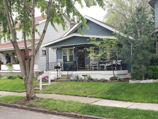 view of front of house featuring covered porch, a chimney, and a front yard
