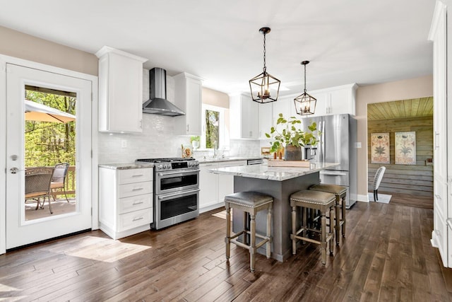 kitchen with wall chimney range hood, a kitchen island, appliances with stainless steel finishes, a breakfast bar, and white cabinetry