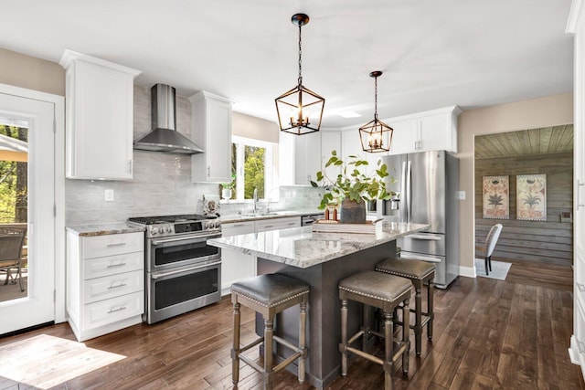 kitchen with white cabinetry, appliances with stainless steel finishes, a breakfast bar area, and wall chimney range hood
