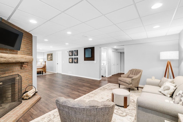 living room featuring baseboards, a brick fireplace, wood finished floors, and a paneled ceiling