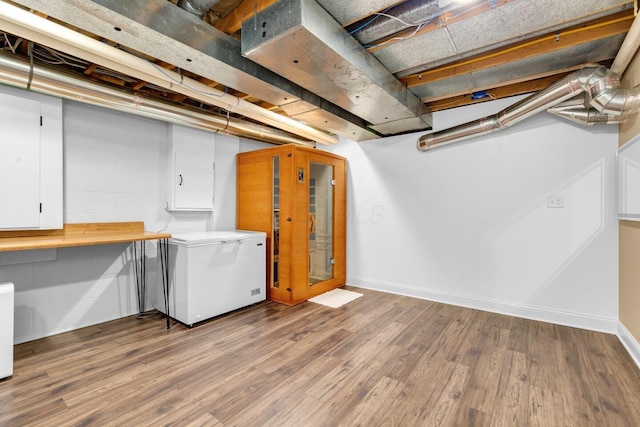 unfinished basement with baseboards, wood finished floors, and refrigerator