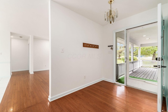 unfurnished room with wood-type flooring, an inviting chandelier, and visible vents
