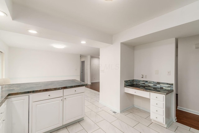 kitchen with white cabinets, recessed lighting, dark countertops, and built in desk
