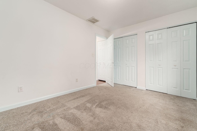 unfurnished bedroom featuring baseboards, carpet, multiple closets, and visible vents