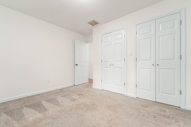 unfurnished bedroom featuring visible vents, carpet flooring, baseboards, and two closets