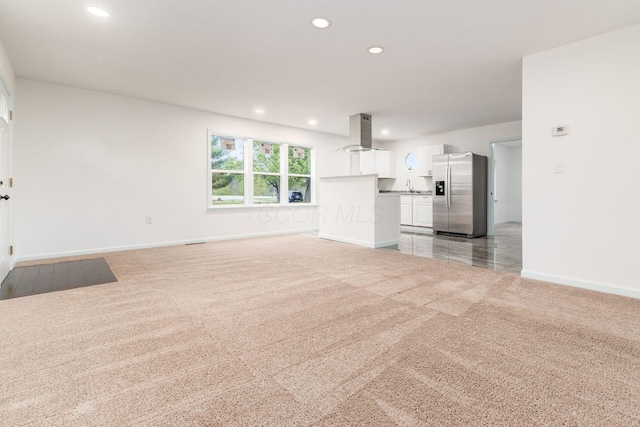 unfurnished living room with recessed lighting, baseboards, light colored carpet, and a sink