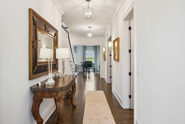 corridor with baseboards, dark wood-style floors, ornamental molding, and an inviting chandelier