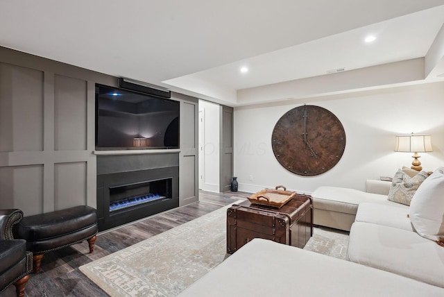 living area featuring a glass covered fireplace, recessed lighting, baseboards, wood finished floors, and visible vents