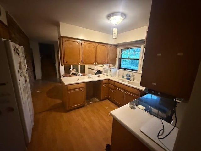 kitchen featuring light countertops, light wood finished floors, white microwave, and brown cabinets