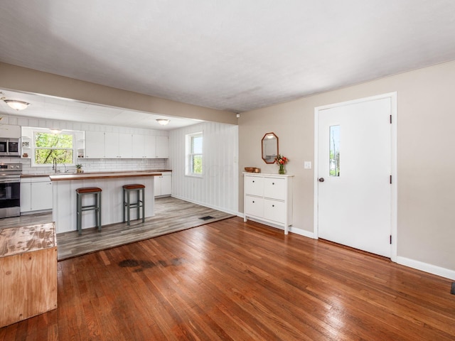 kitchen with stainless steel appliances, white cabinetry, wood finished floors, and a kitchen bar