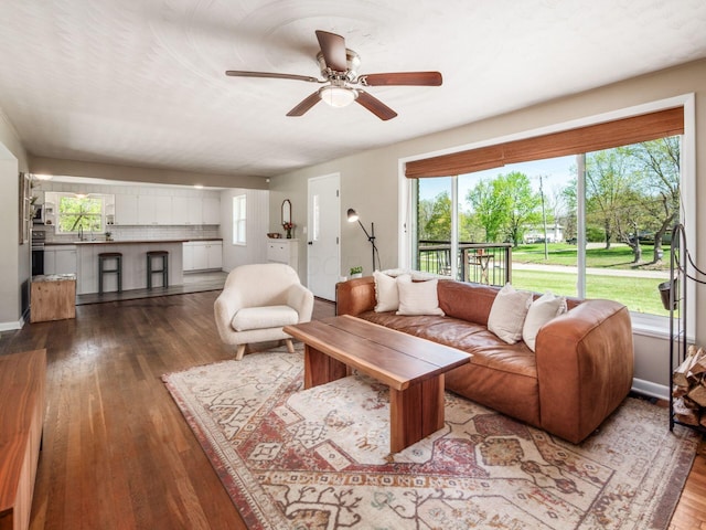 living area featuring wood-type flooring, a ceiling fan, and baseboards