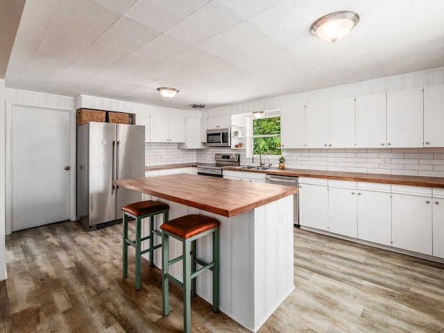 kitchen with wooden counters, appliances with stainless steel finishes, a sink, light wood-style floors, and white cabinetry