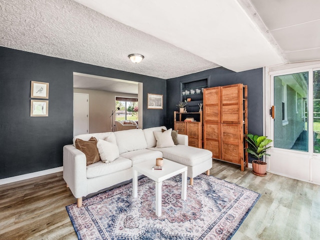 living area featuring built in features, baseboards, a textured ceiling, and wood finished floors