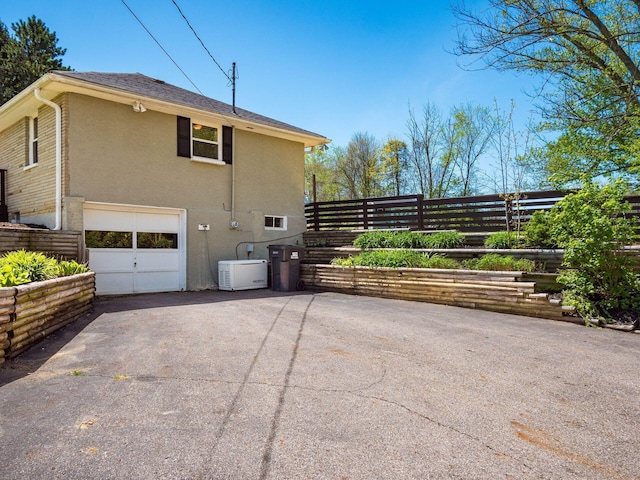 view of property exterior featuring fence, an attached garage, and driveway