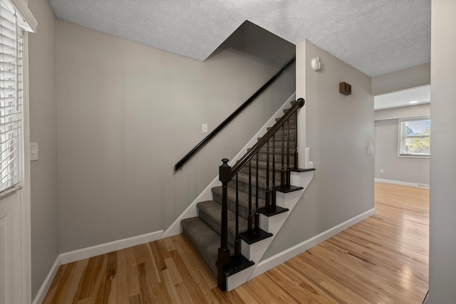 stairway featuring baseboards, a textured ceiling, and wood finished floors