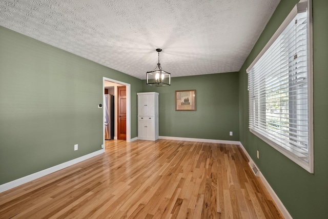 unfurnished dining area with a textured ceiling, visible vents, baseboards, a chandelier, and light wood-style floors