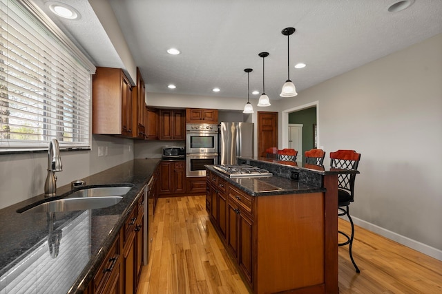 kitchen with a breakfast bar area, stainless steel appliances, a sink, and light wood-style floors