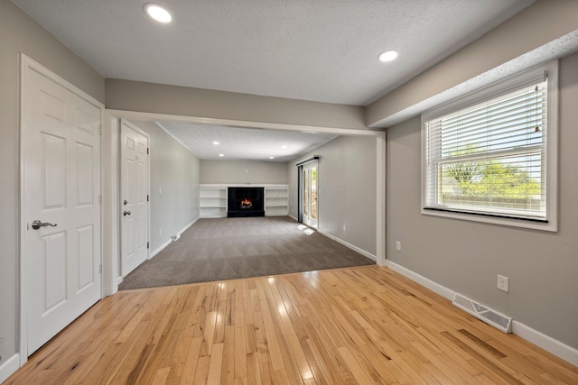 unfurnished living room featuring visible vents, wood-type flooring, baseboards, and a lit fireplace