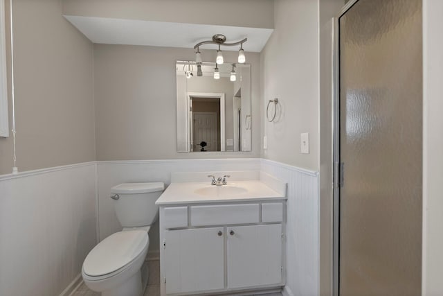 bathroom with vanity, toilet, wainscoting, and a stall shower