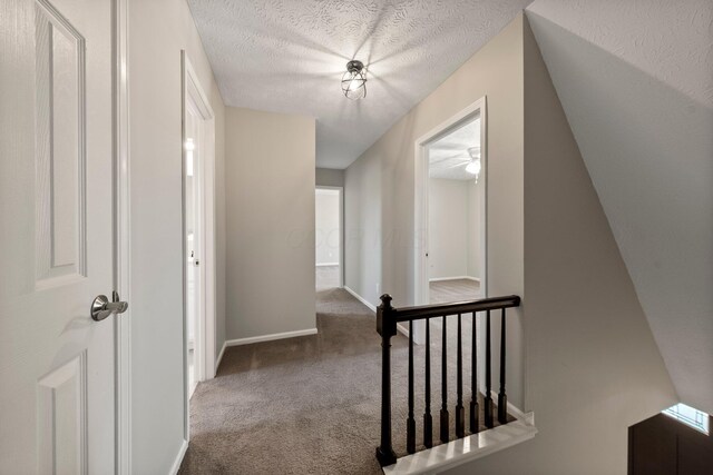 hallway featuring carpet floors, a textured ceiling, baseboards, and an upstairs landing