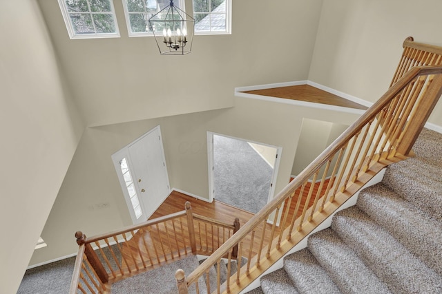 stairway featuring a wealth of natural light, a chandelier, baseboards, and a high ceiling