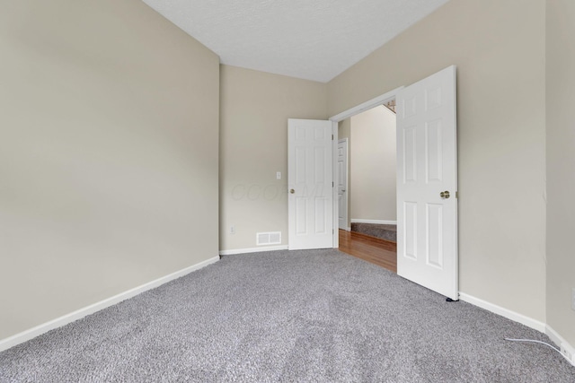 unfurnished bedroom with carpet, a textured ceiling, visible vents, and baseboards