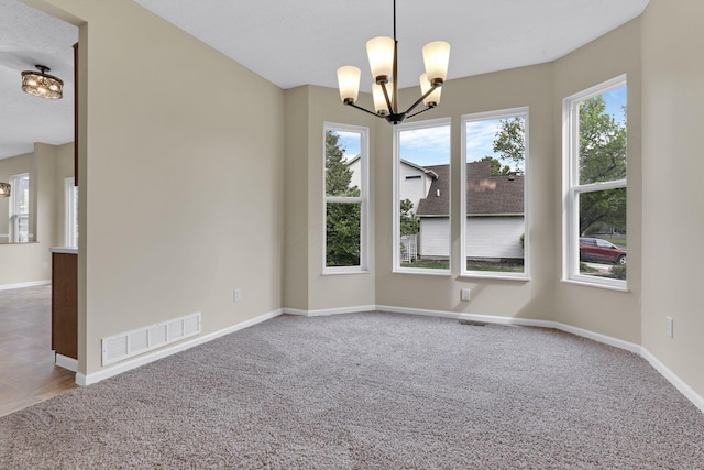 empty room with carpet floors, an inviting chandelier, baseboards, and visible vents