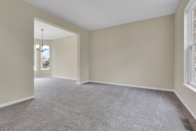 spare room with carpet, a notable chandelier, and plenty of natural light