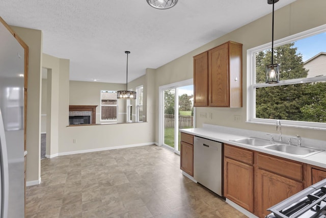 kitchen with stainless steel dishwasher, a wealth of natural light, a glass covered fireplace, and brown cabinets