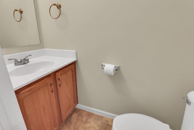 half bath with toilet, baseboards, and vanity