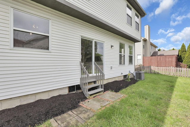 view of property exterior with a lawn, central AC unit, fence, and entry steps