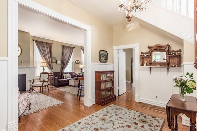 interior space featuring a tiled fireplace, wood finished floors, a notable chandelier, and a wainscoted wall