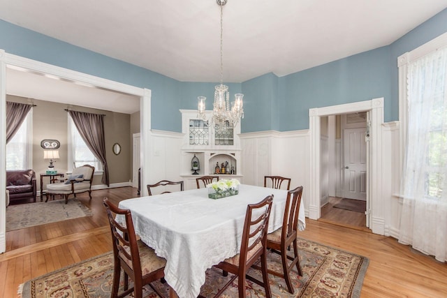 dining area featuring an inviting chandelier, wainscoting, a decorative wall, and light wood-style floors