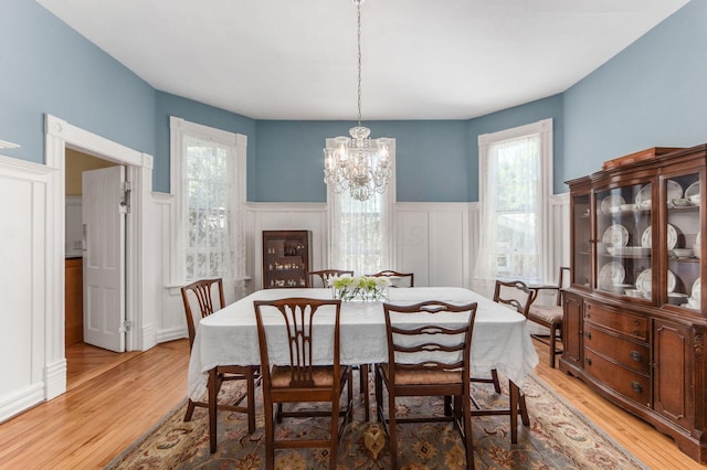 dining area featuring a wainscoted wall, a decorative wall, light wood-style flooring, and a notable chandelier