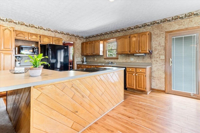 kitchen with a textured ceiling, wallpapered walls, a sink, and black appliances