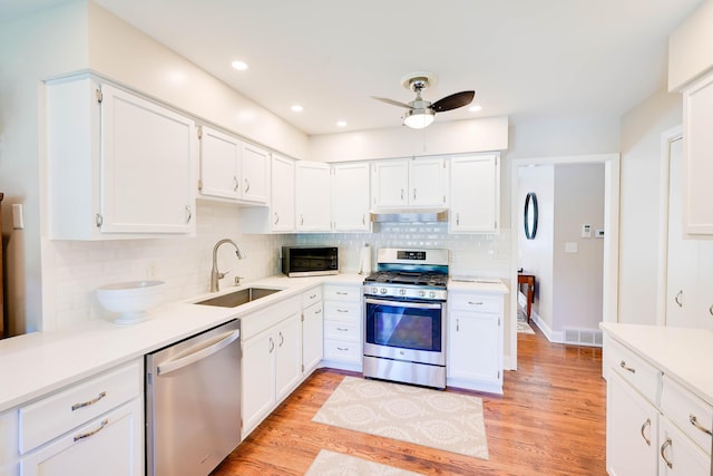 kitchen with white cabinetry, under cabinet range hood, tasteful backsplash, a sink, and appliances with stainless steel finishes