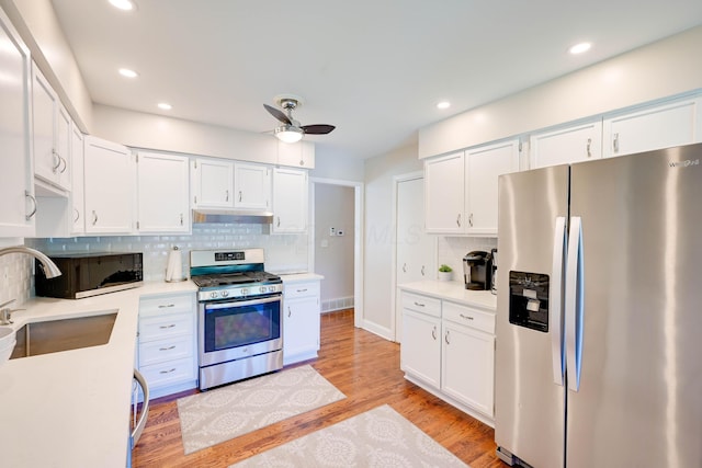 kitchen with appliances with stainless steel finishes, a sink, a ceiling fan, tasteful backsplash, and under cabinet range hood