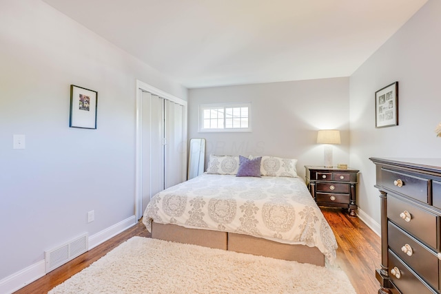 bedroom with baseboards, a closet, wood finished floors, and visible vents