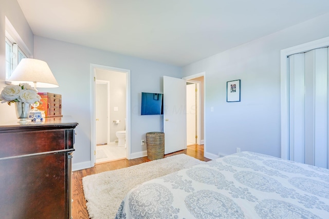 bedroom with baseboards, ensuite bath, wood finished floors, and a closet