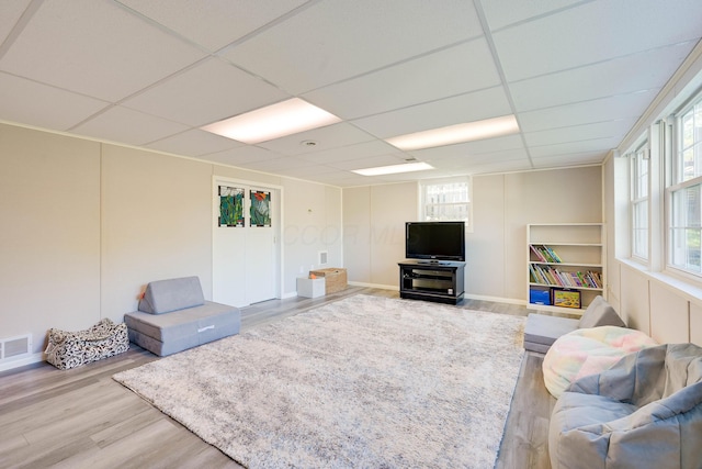 living area featuring wood finished floors, plenty of natural light, a drop ceiling, and visible vents