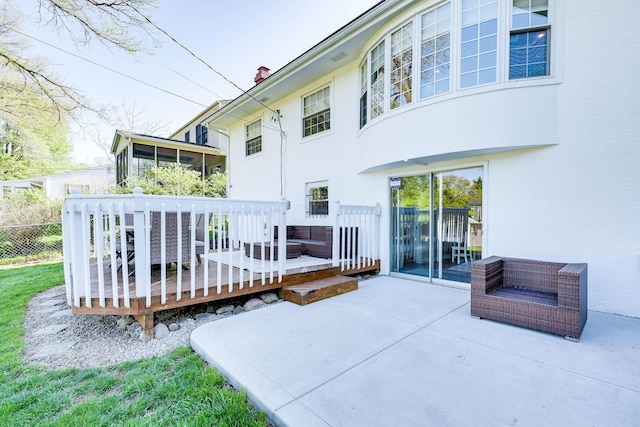 back of property featuring a wooden deck, a sunroom, fence, a patio, and stucco siding