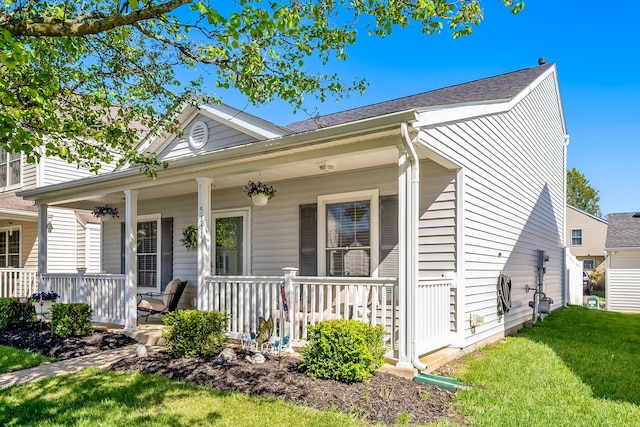 bungalow-style house featuring a front lawn, roof with shingles, and covered porch