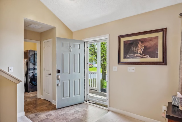foyer entrance featuring stacked washing maching and dryer, stone finish floor, baseboards, and vaulted ceiling